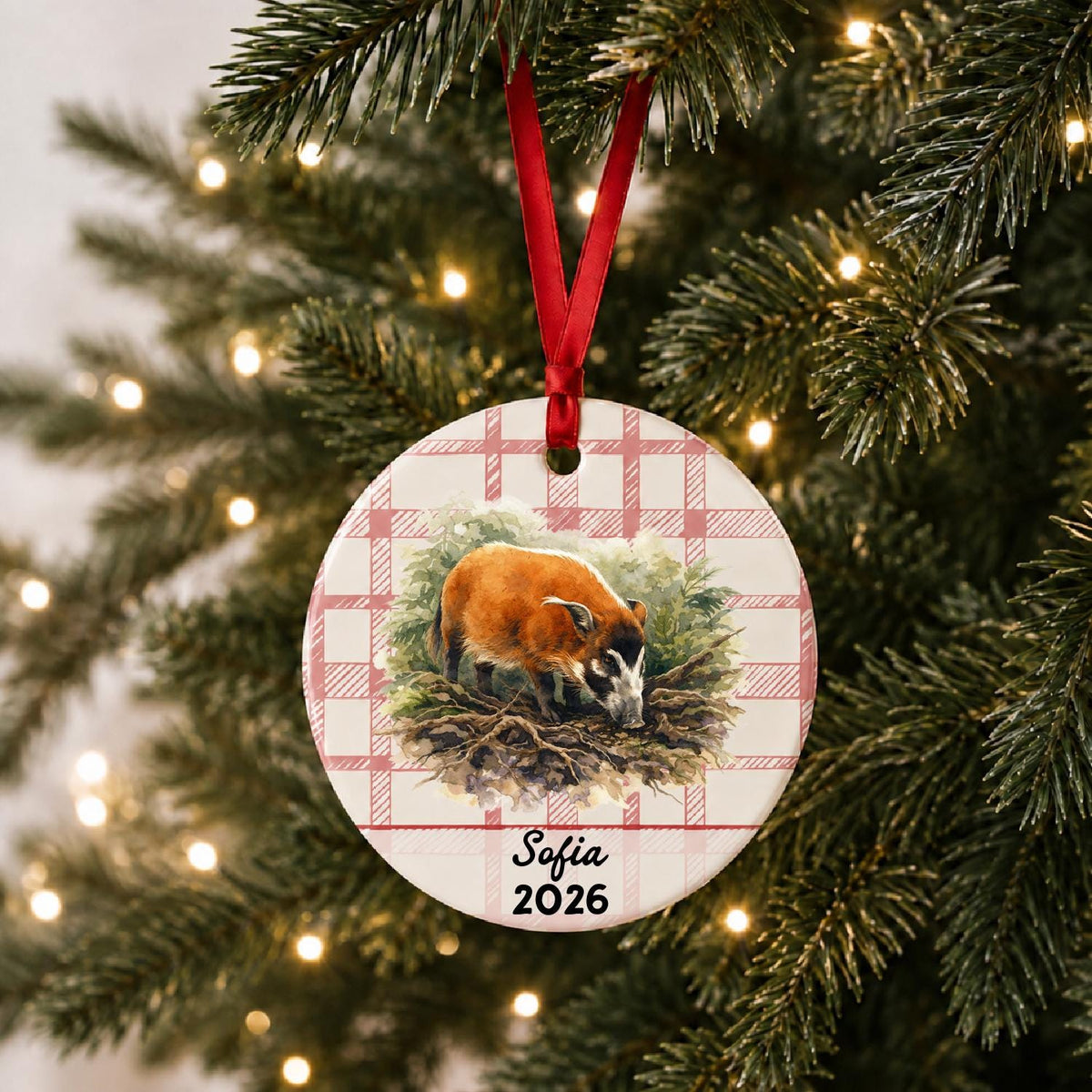 Personalized red river hog in forest ceramic ornament with name and year on red plaid hanging on a lit Christmas tree