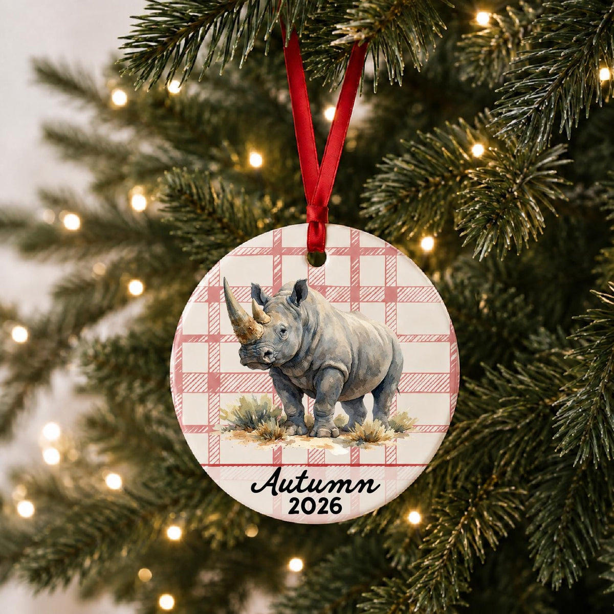 Personalized white rhinoceros in grassland ceramic ornament with name and year on red plaid hanging on a lit Christmas tree