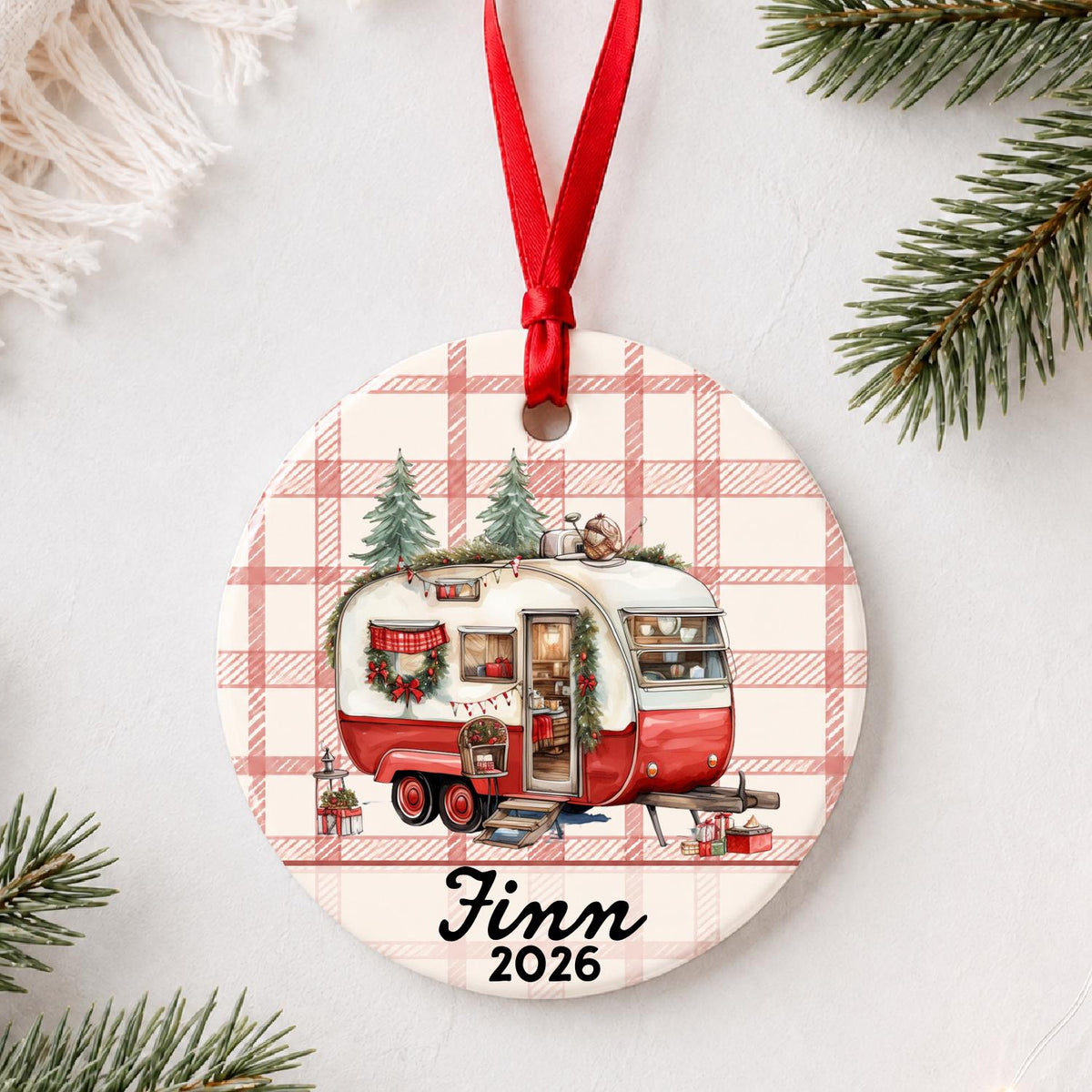 Vintage camper ceramic ornament personalized Finn 2026, hanging by a red ribbon in a Christmas flat lay