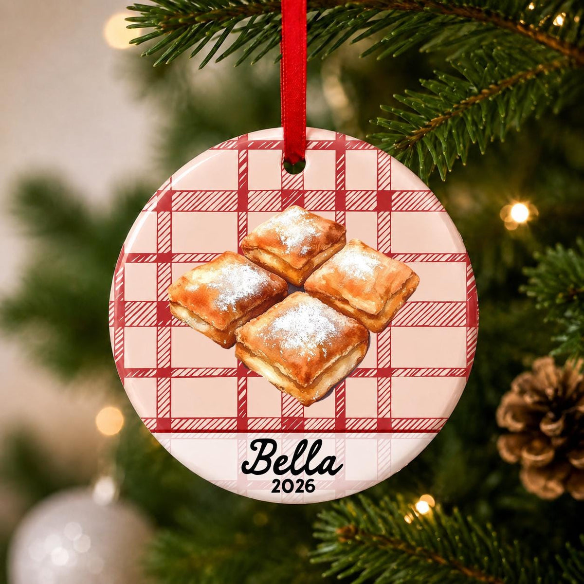 Close-up of the personalized beignets ceramic ornament with name and year on red plaid hanging on a Christmas tree