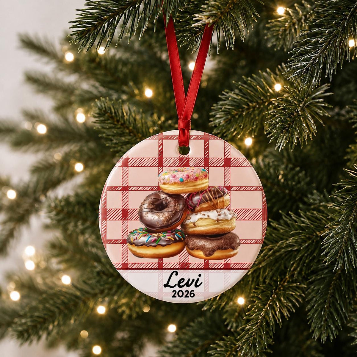 Personalized donuts ceramic ornament with name and year on red plaid hanging on a lit Christmas tree