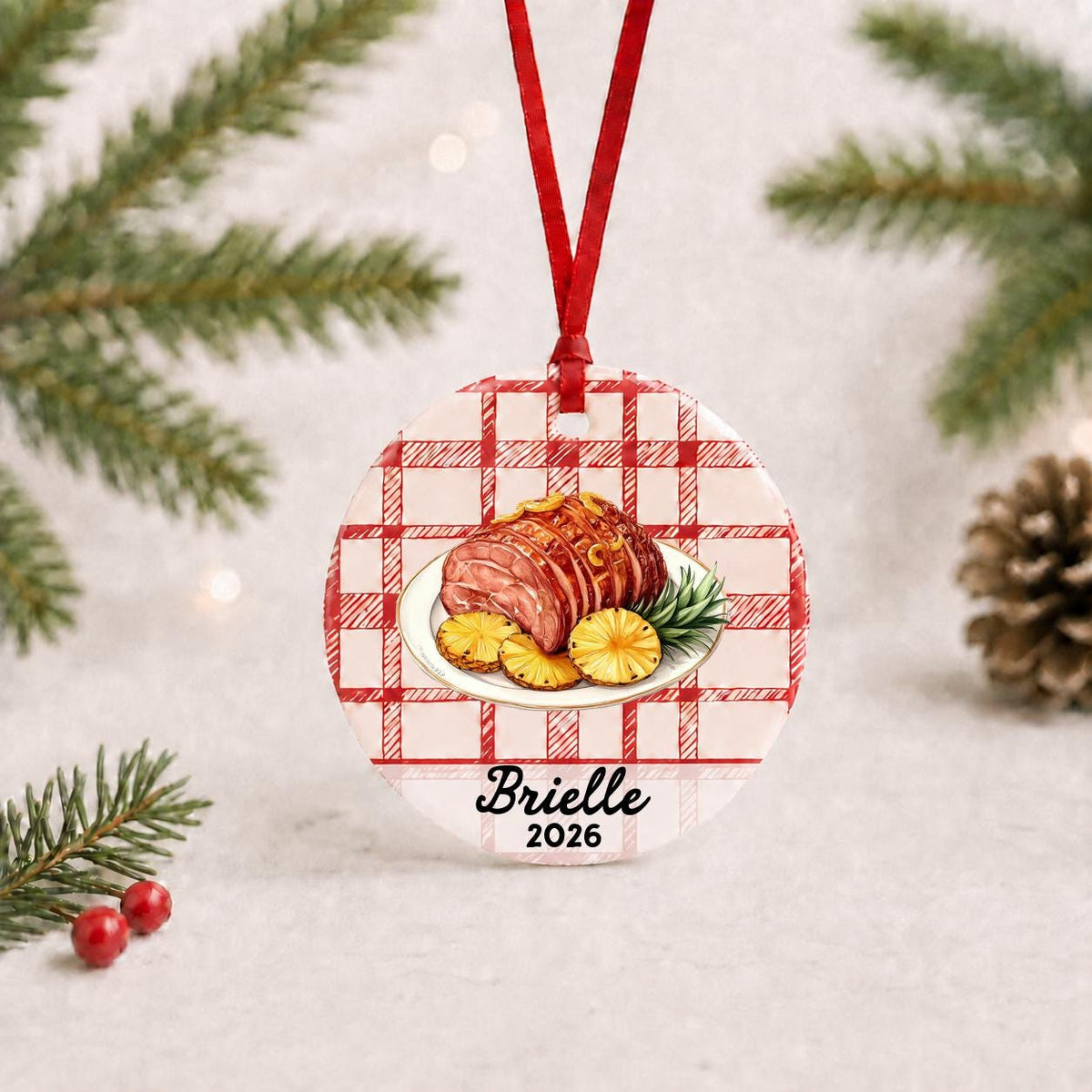 Personalized Christmas ham ceramic ornament with name and year on red plaid with red ribbon on a white surface with pine branches and pinecones