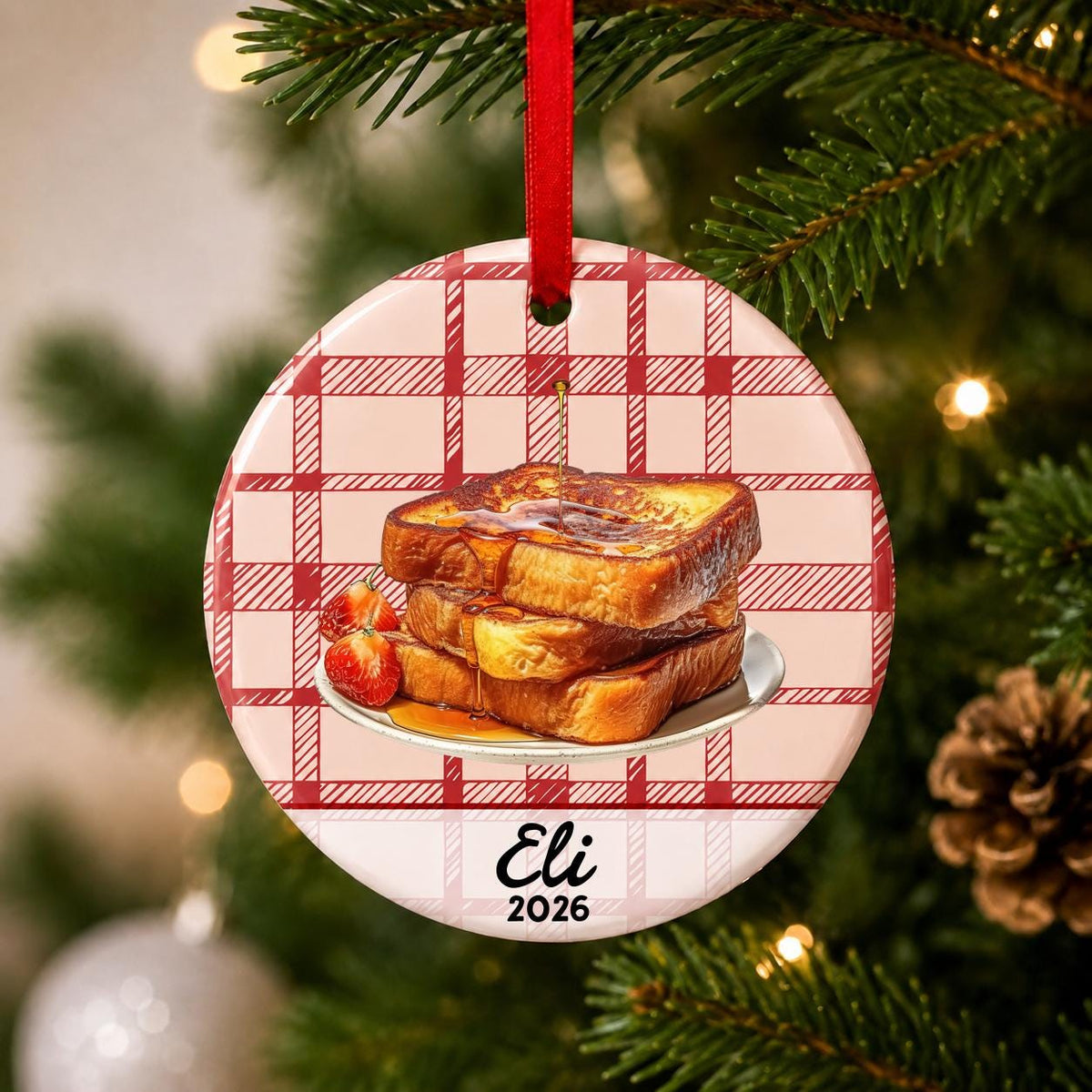 Close-up of the personalized French toast ceramic ornament with name and year on red plaid hanging on a Christmas tree