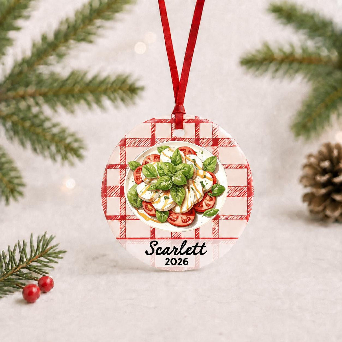 Personalized caprese salad ceramic ornament with name and year on red plaid with red ribbon on a white surface with pine branches and pinecones
