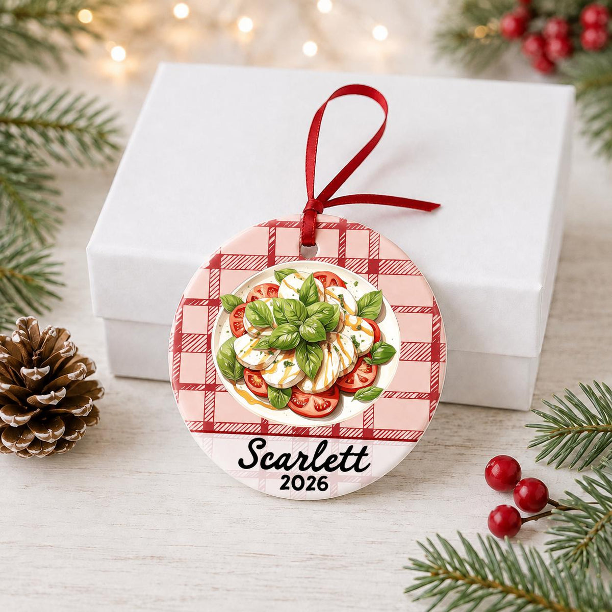 Personalized caprese salad ceramic ornament with name and year on red plaid in front of a white gift box with pinecones and red berries