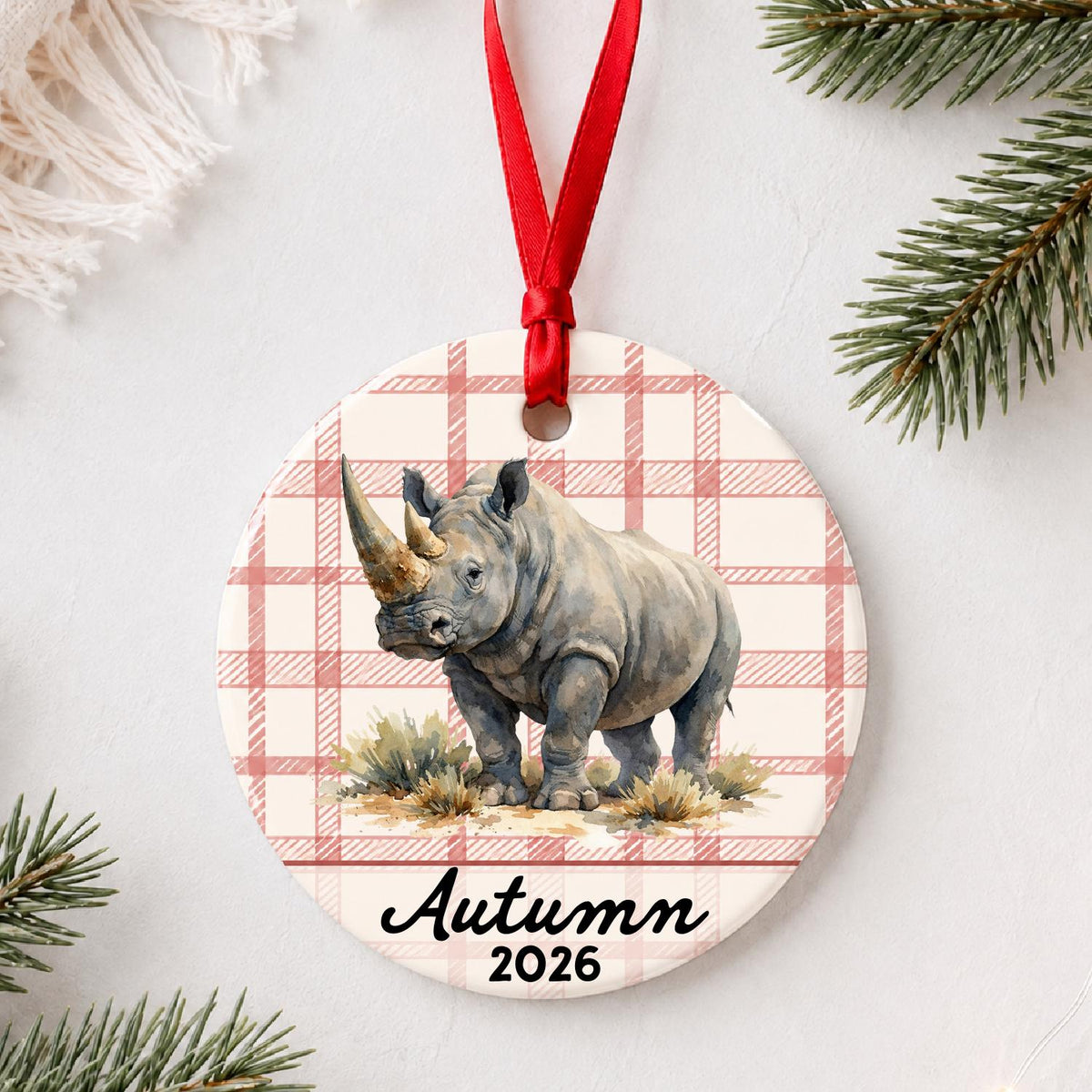 Personalized white rhinoceros in grassland ceramic ornament with name and year on red plaid styled with pine branches on a soft white background
