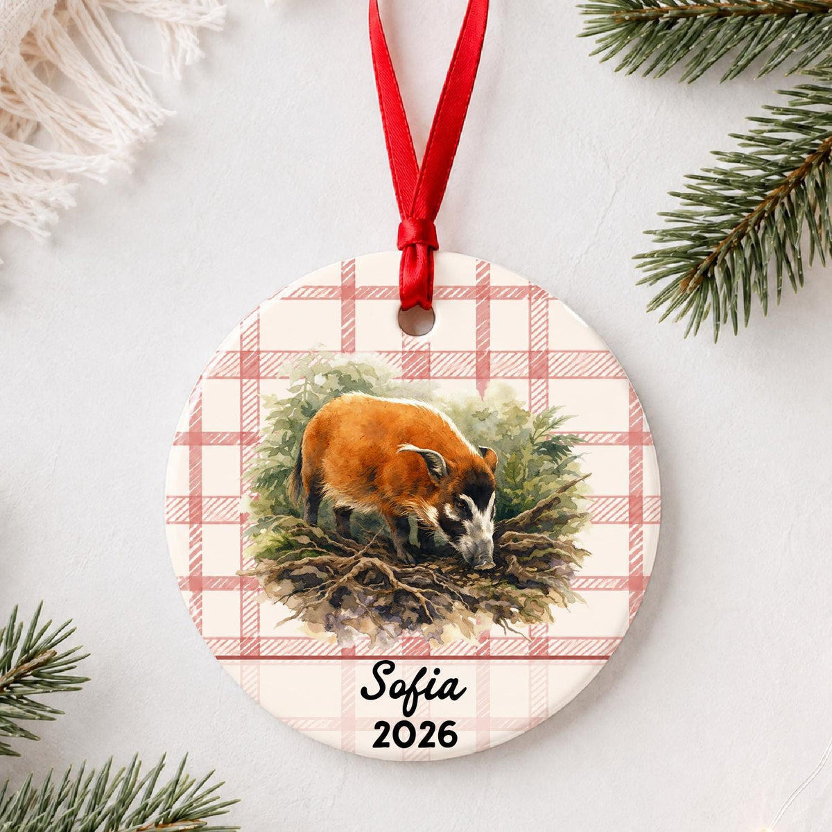 Personalized red river hog in forest ceramic ornament with name and year on red plaid styled with pine branches on a soft white background