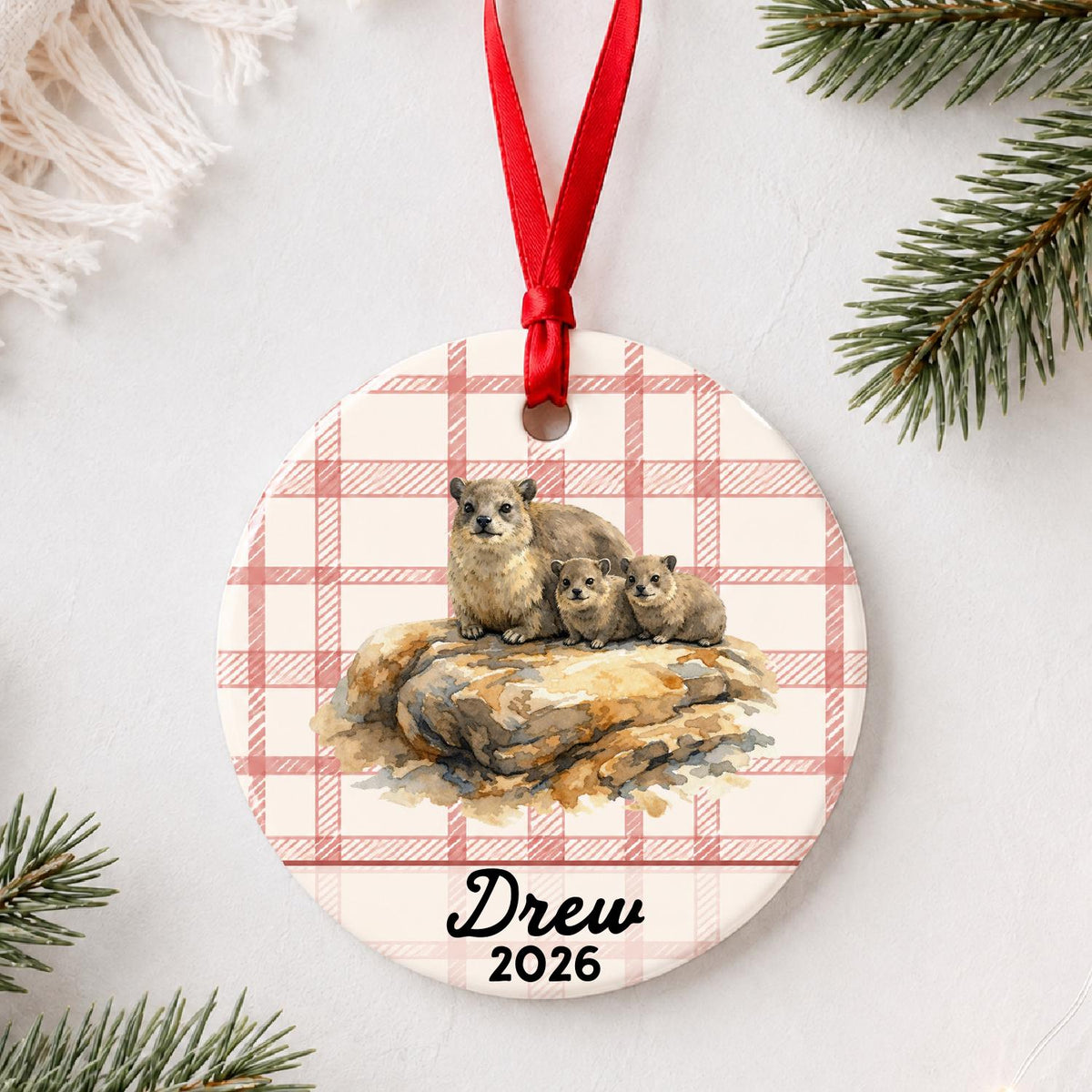 Personalized rock hyraxes ceramic ornament with name and year on red plaid styled with pine branches on a soft white background