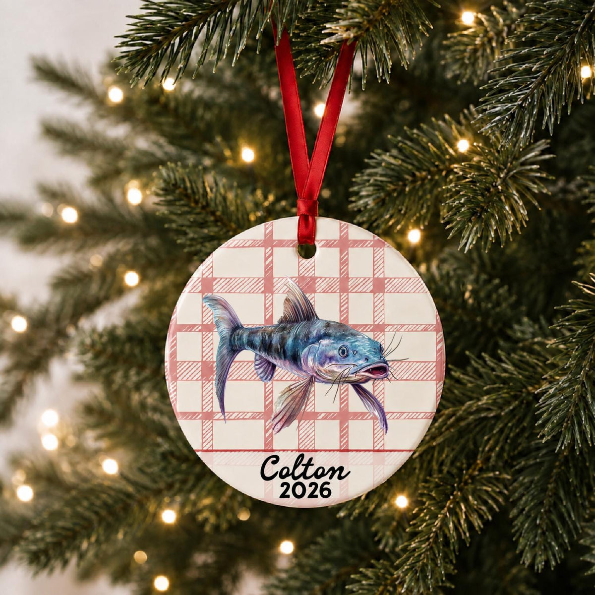 Personalized catfish ceramic ornament with name and year on red plaid hanging on a lit Christmas tree