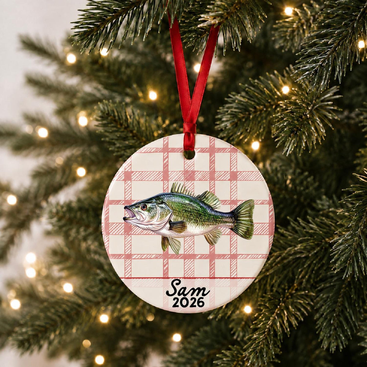 Personalized largemouth bass ceramic ornament with name and year on red plaid hanging on a lit Christmas tree