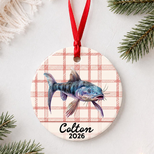 Personalized catfish ceramic ornament with name and year on red plaid styled with pine branches on a soft white background