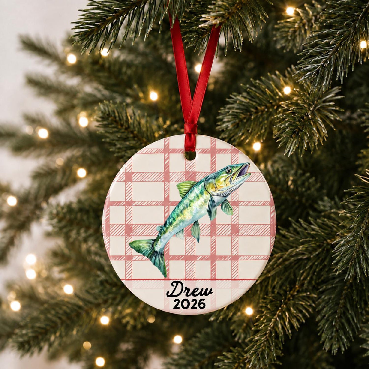 Personalized muskie ceramic ornament with name and year on red plaid hanging on a lit Christmas tree