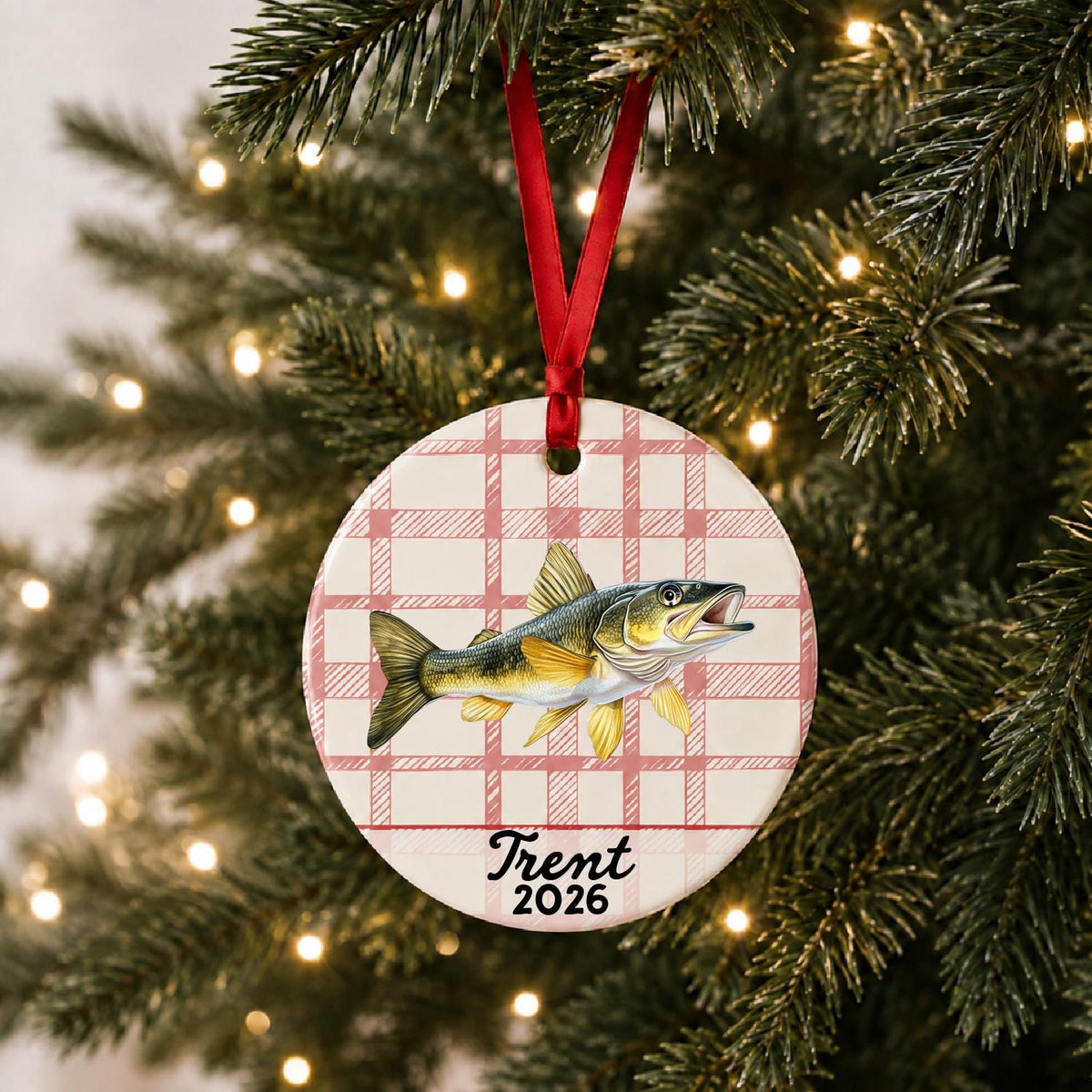 Personalized golden walleye ceramic ornament with name and year on red plaid hanging on a lit Christmas tree
