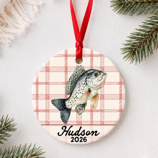 Personalized crappie ceramic ornament with name and year on red plaid styled with pine branches on a soft white background