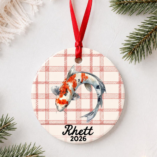 Personalized koi fish ceramic ornament with name and year on red plaid styled with pine branches on a soft white background