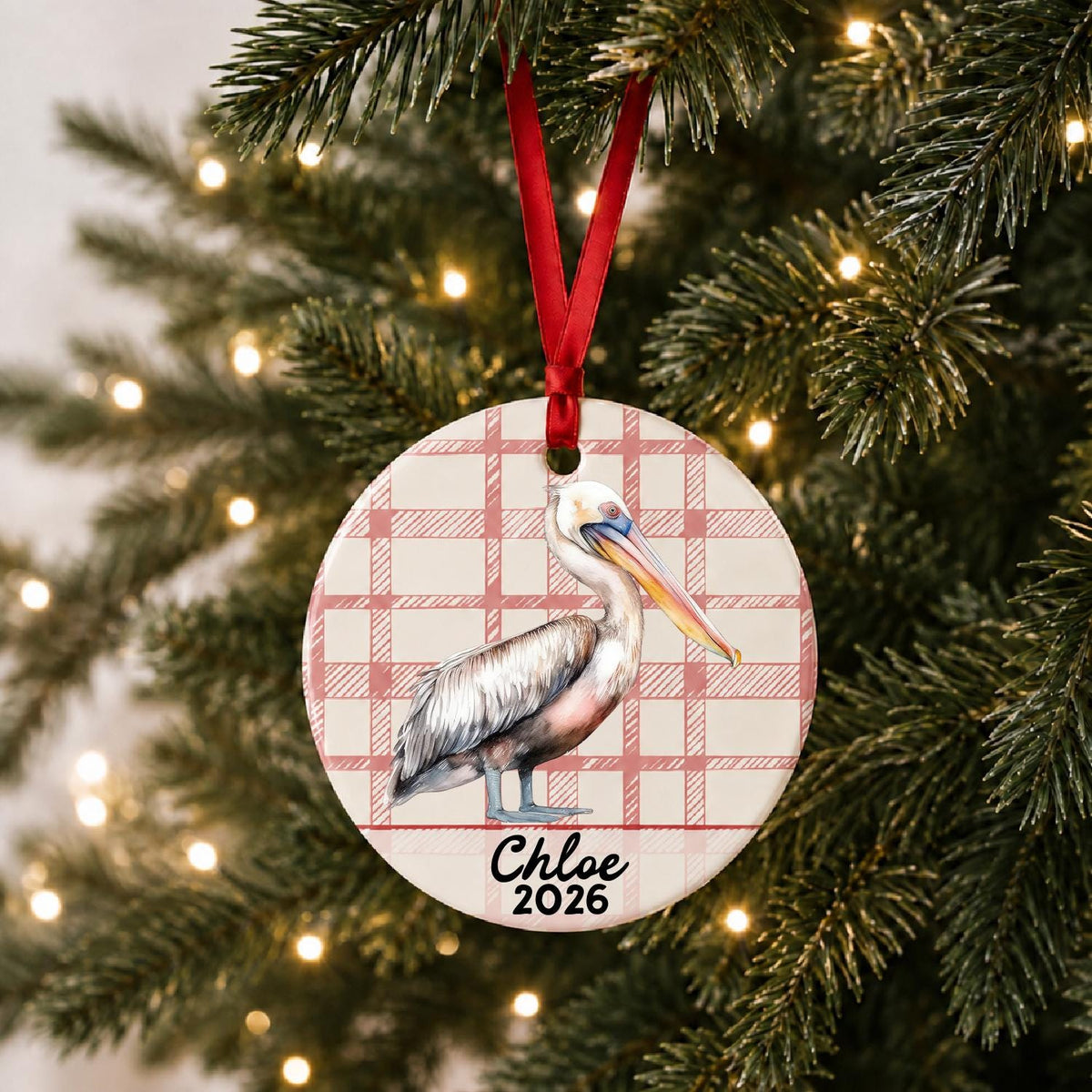 Personalized pelican ceramic ornament with name and year on red plaid hanging on a lit Christmas tree