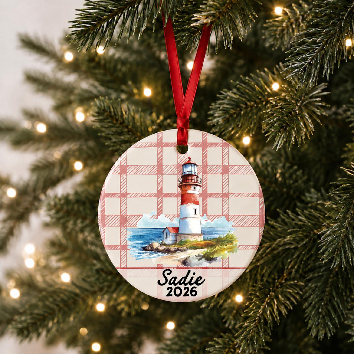 Personalized beach lighthouse ceramic ornament with name and year on red plaid hanging on a lit Christmas tree