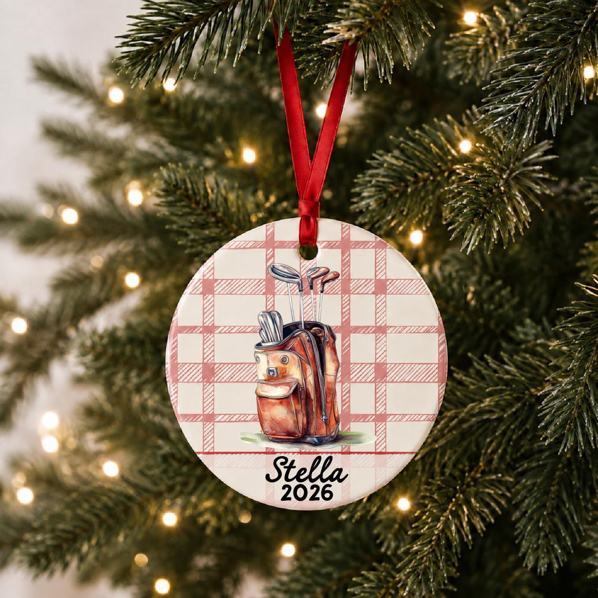 Personalized golf bag ceramic ornament with name and year on red plaid hanging on a lit Christmas tree