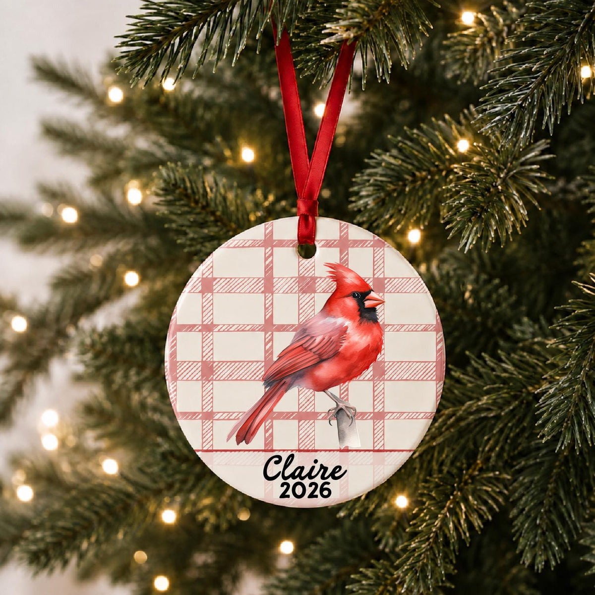 Personalized northern cardinal ceramic ornament with name and year on red plaid hanging on a lit Christmas tree