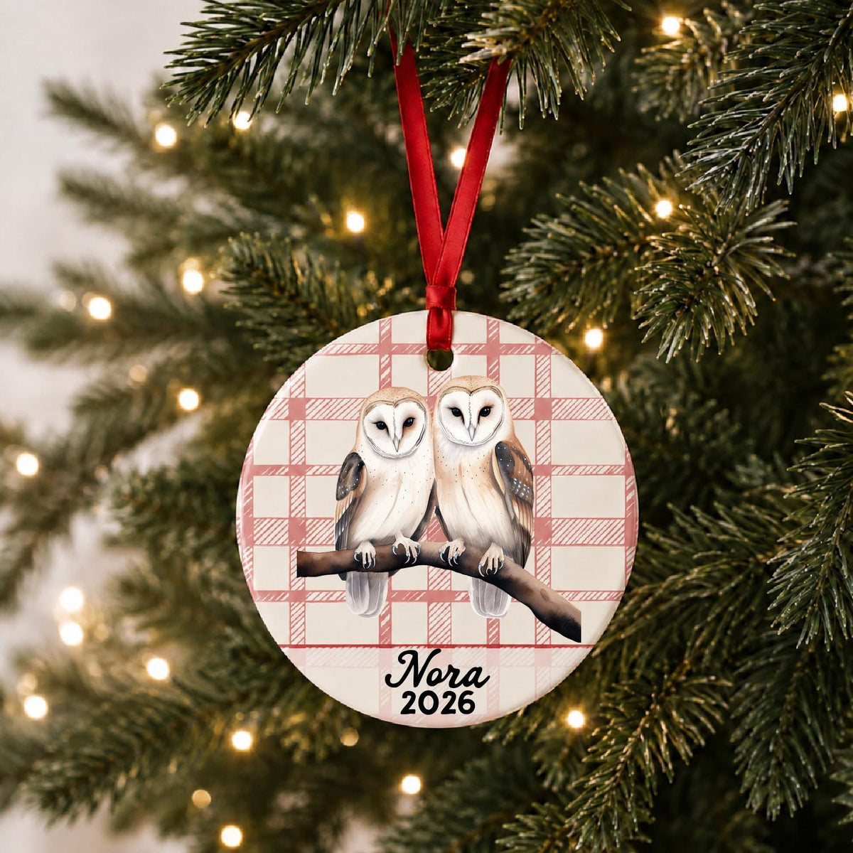 Personalized barn owl pair ceramic ornament with name and year on red plaid hanging on a lit Christmas tree