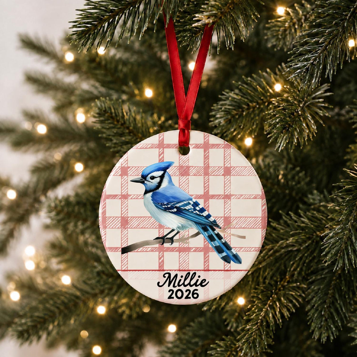 Personalized blue jay ceramic ornament with name and year on red plaid hanging on a lit Christmas tree
