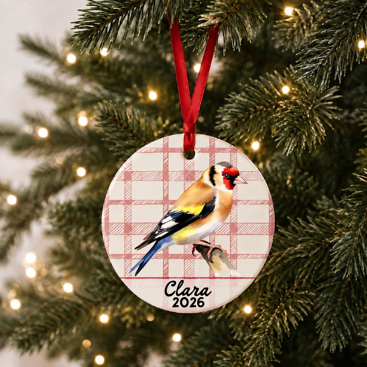 Personalized European goldfinch ceramic ornament with name and year on red plaid hanging on a lit Christmas tree