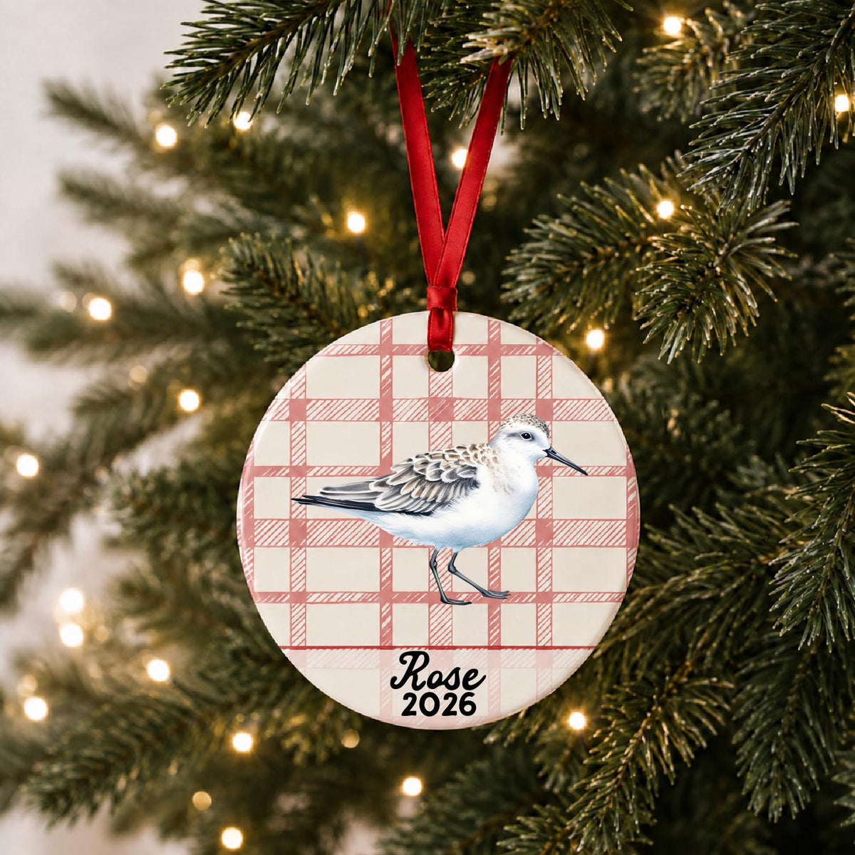 Personalized sanderling ceramic ornament with name and year on red plaid hanging on a lit Christmas tree