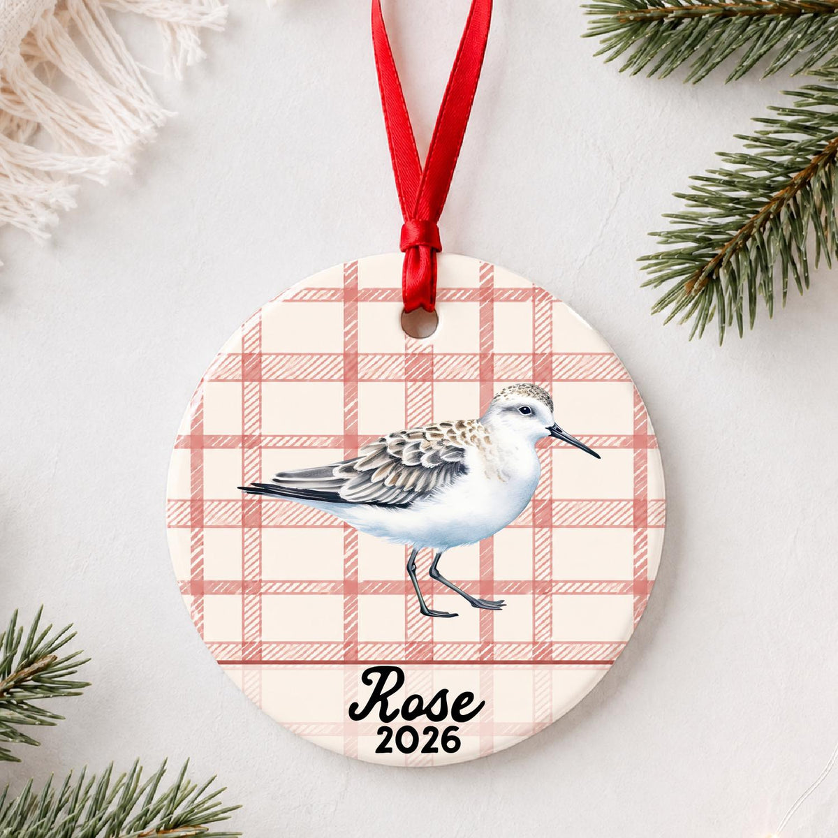 Personalized sanderling ceramic ornament with name and year on red plaid styled with pine branches on a soft white background