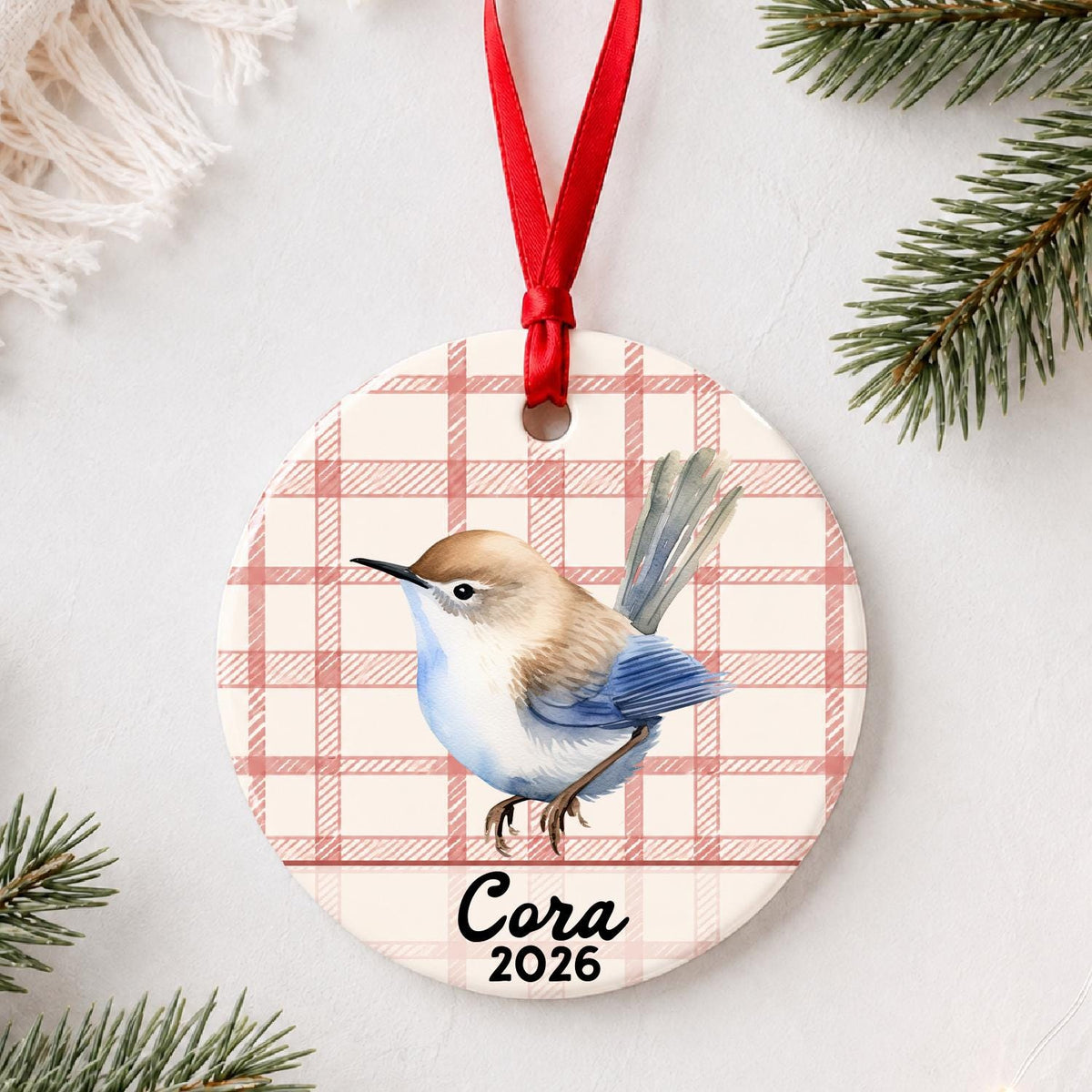 Personalized wren ceramic ornament with name and year on red plaid styled with pine branches on a soft white background