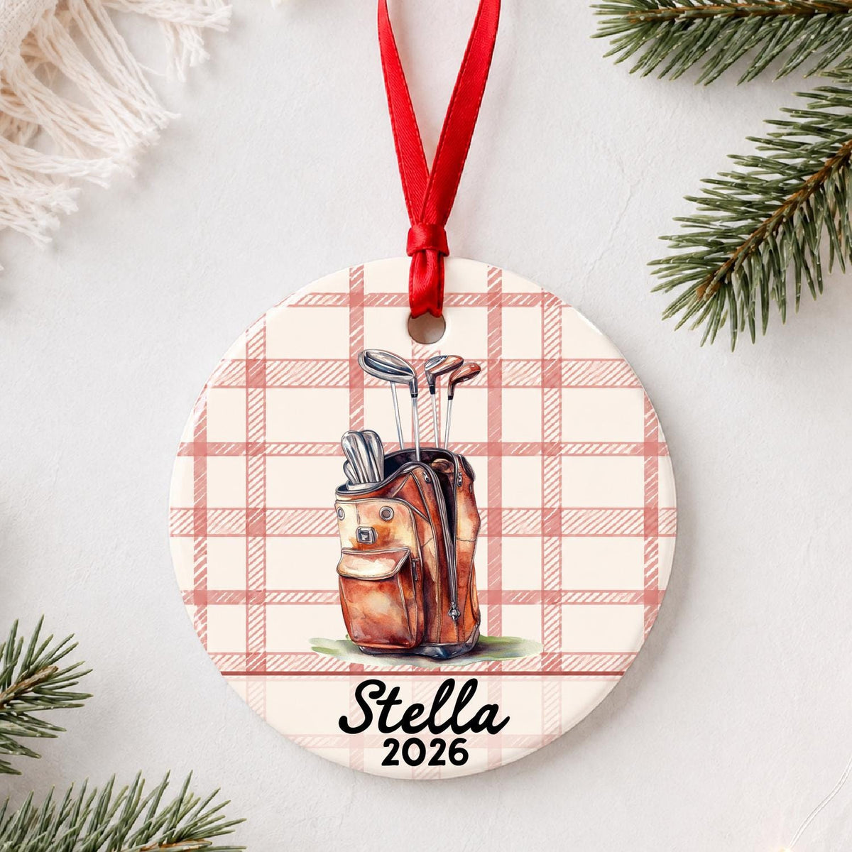 Personalized golf bag ceramic ornament with name and year on red plaid styled with pine branches on a soft white background