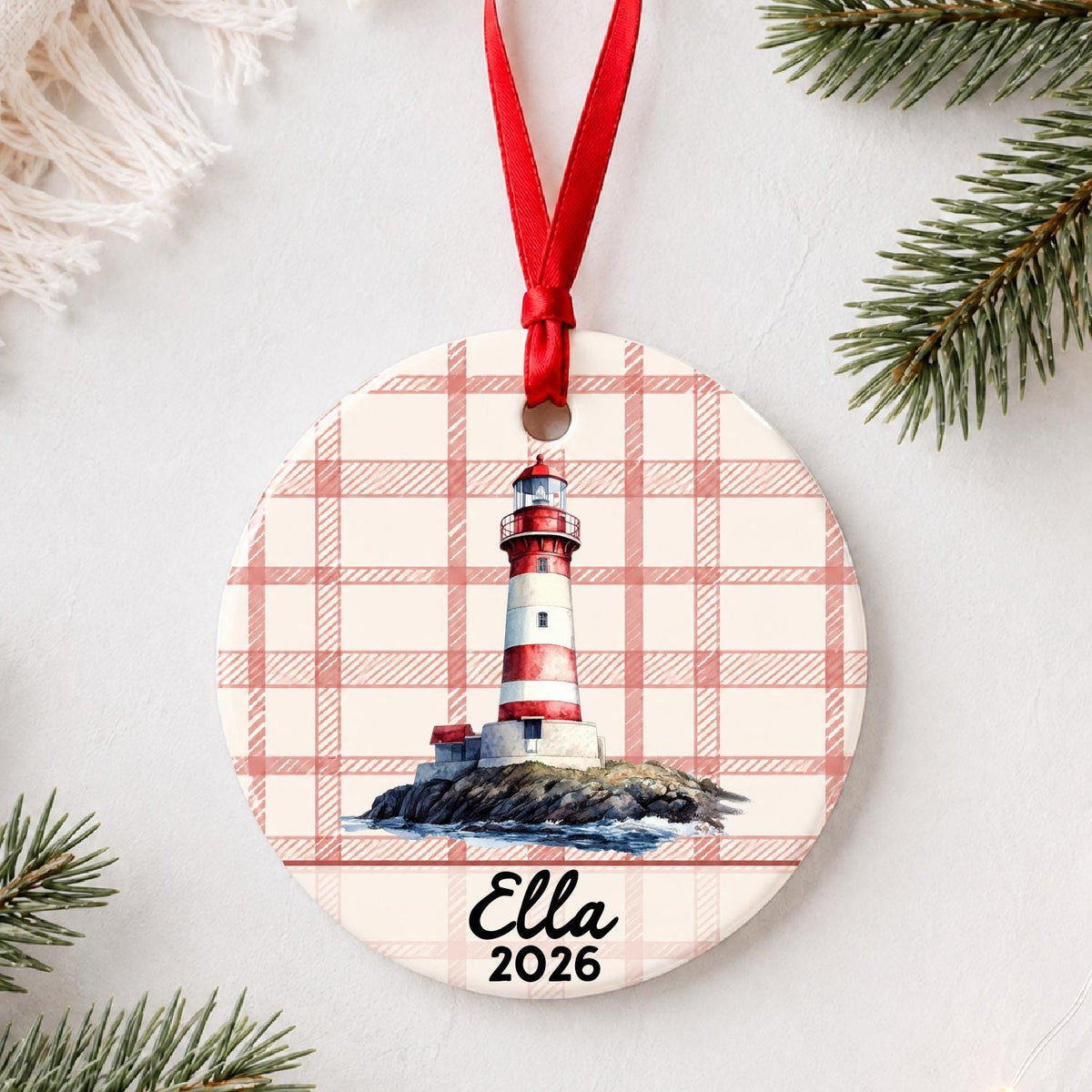 Personalized island lighthouse ceramic ornament with name and year on red plaid styled with pine branches on a soft white background