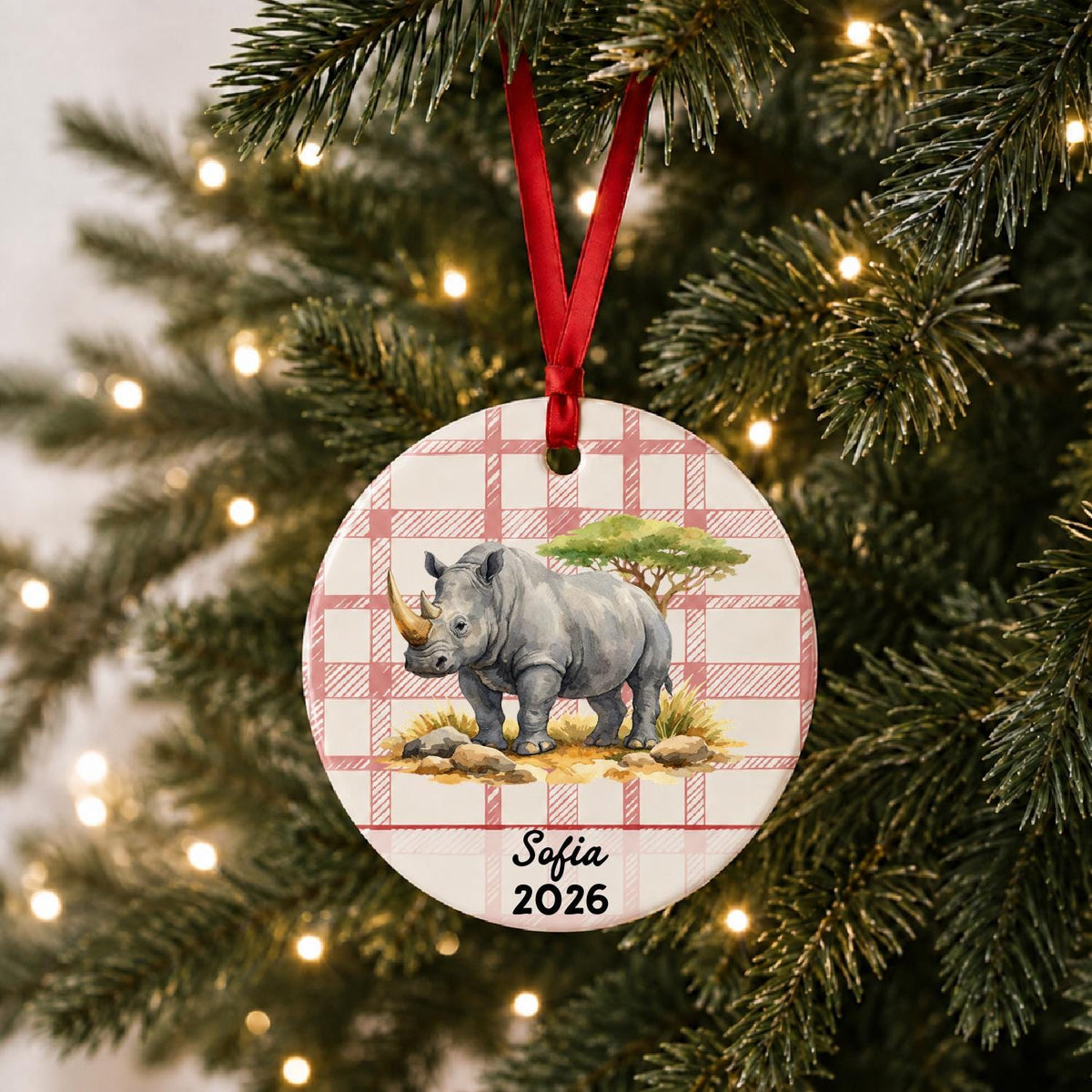 Personalized white rhinoceros ceramic ornament with name and year on red plaid hanging on a lit Christmas tree