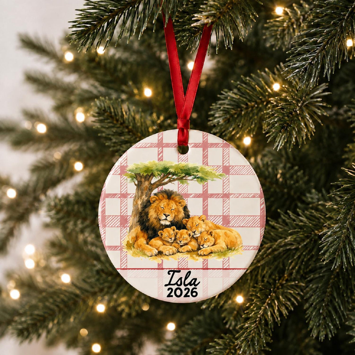 Personalized lion pride ceramic ornament with name and year on red plaid hanging on a lit Christmas tree