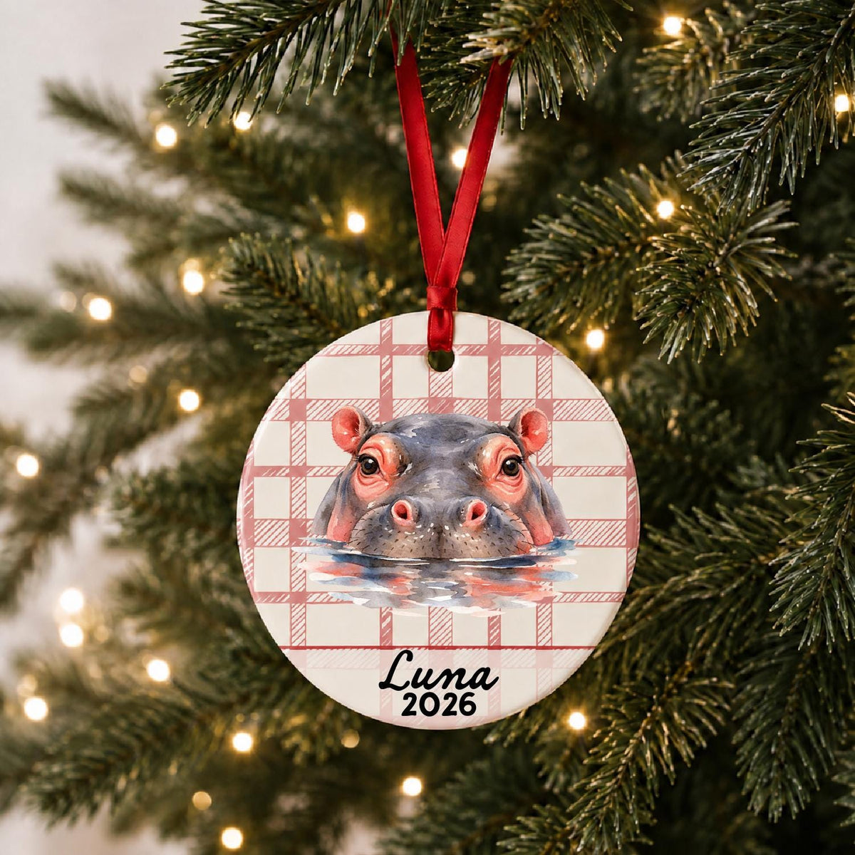 Personalized hippopotamus ceramic ornament with name and year on red plaid hanging on a lit Christmas tree