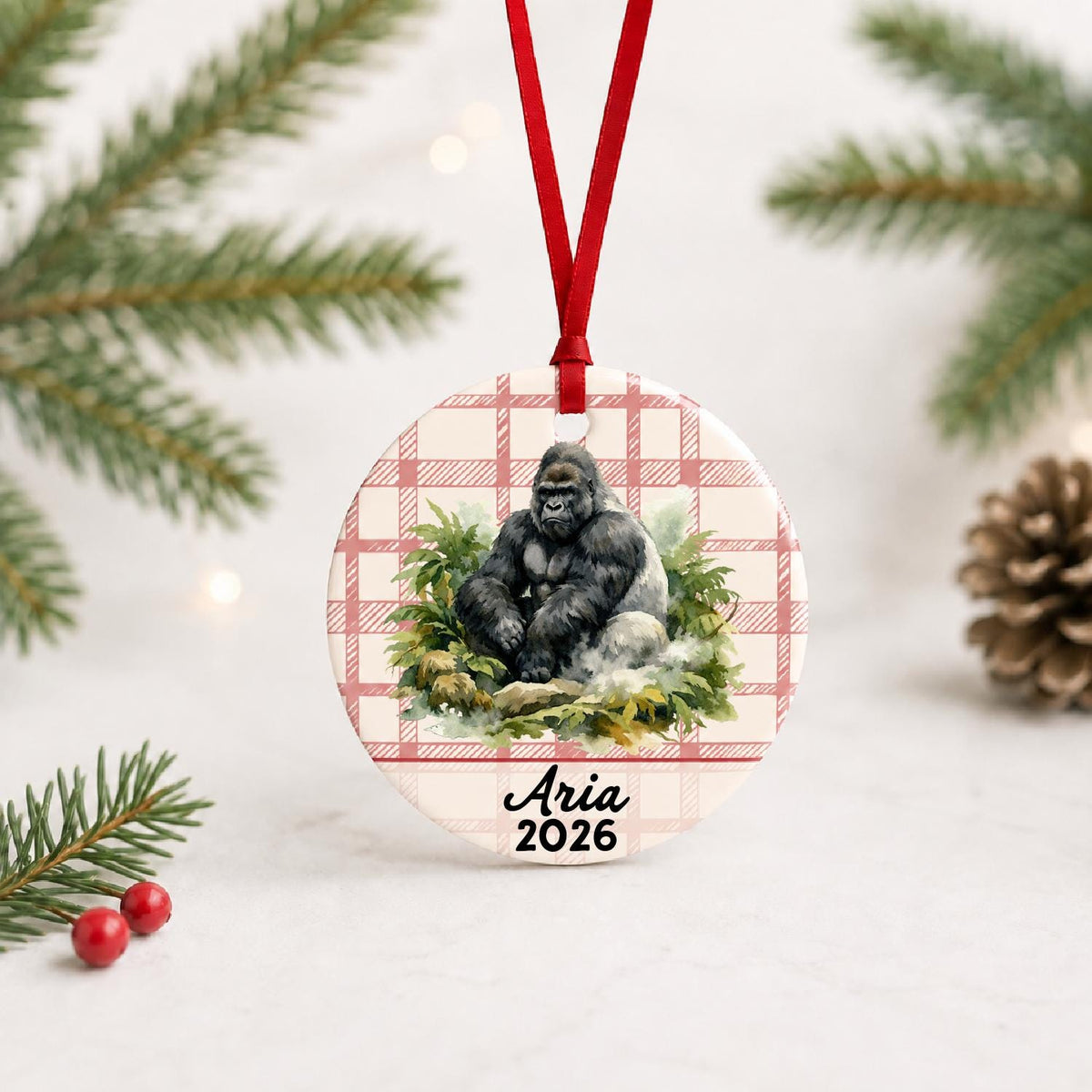 Personalized silverback gorilla ceramic ornament with name and year on red plaid with red ribbon on a white surface with pine branches and pinecones