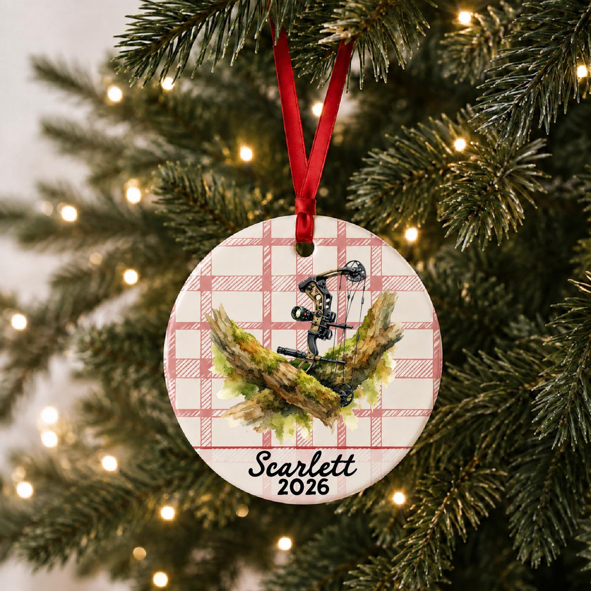 Personalized compound bow ceramic ornament with name and year on red plaid hanging on a lit Christmas tree