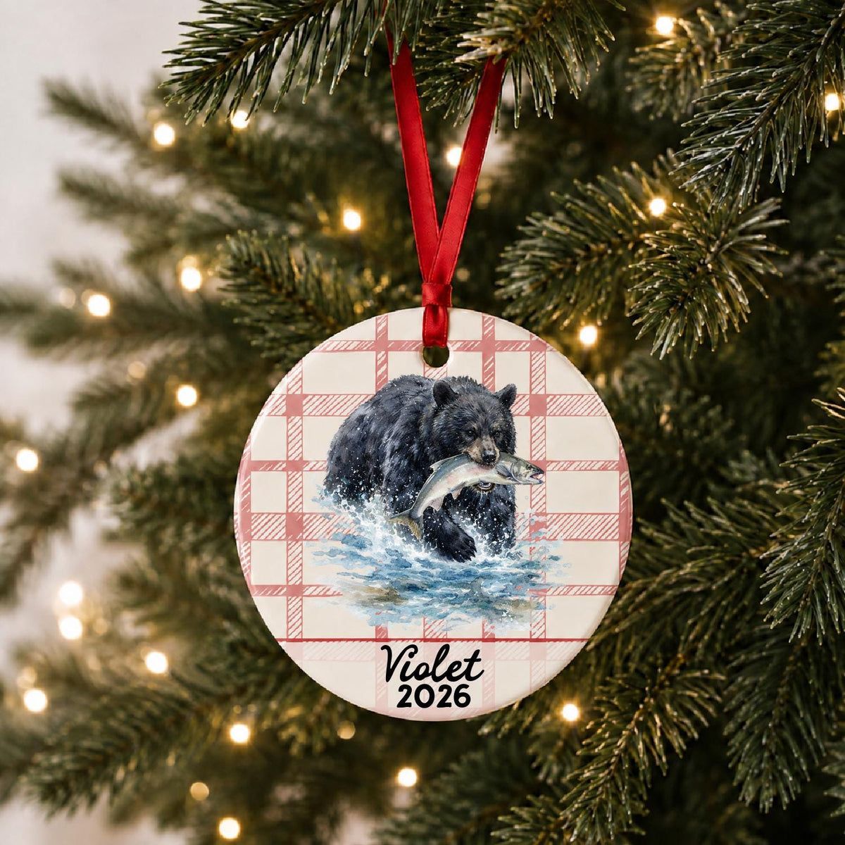 Personalized American black bear ceramic ornament with name and year on red plaid hanging on a lit Christmas tree