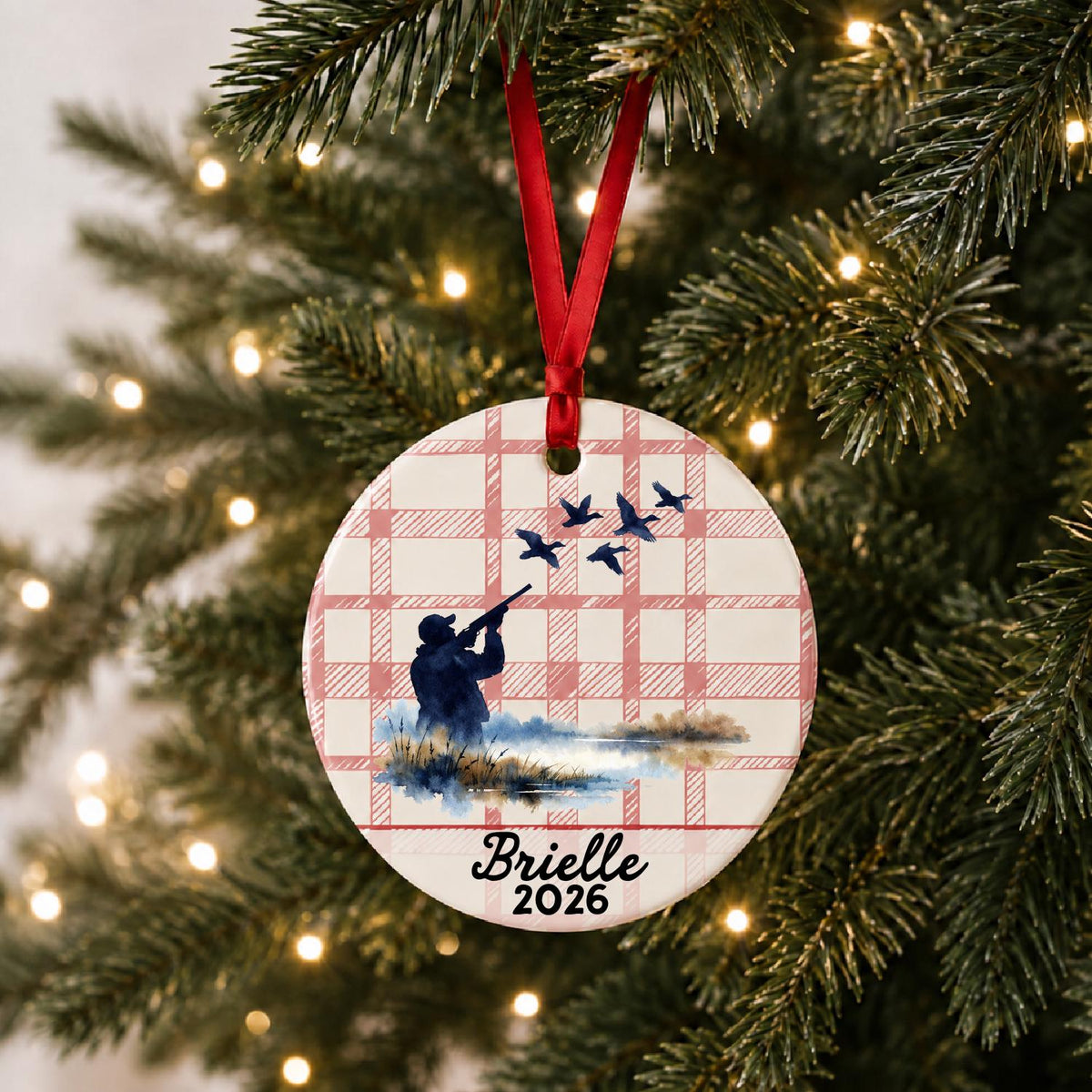 Personalized duck hunting ceramic ornament with name and year on red plaid hanging on a lit Christmas tree