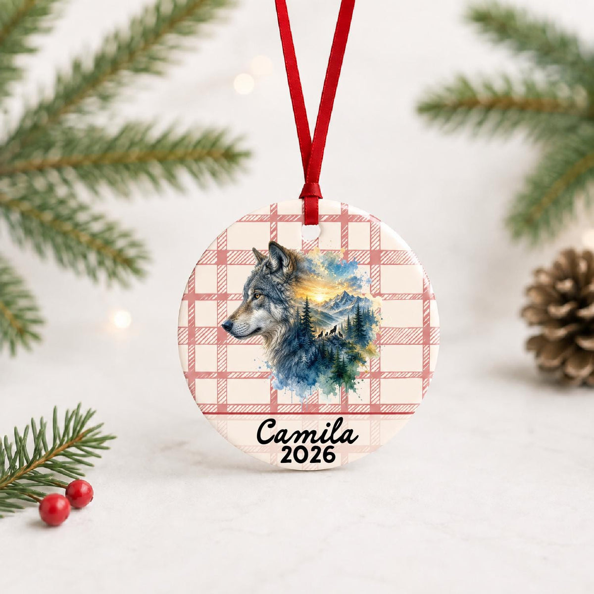 Personalized grey wolf ceramic ornament with name and year on red plaid with red ribbon on a white surface with pine branches and pinecones