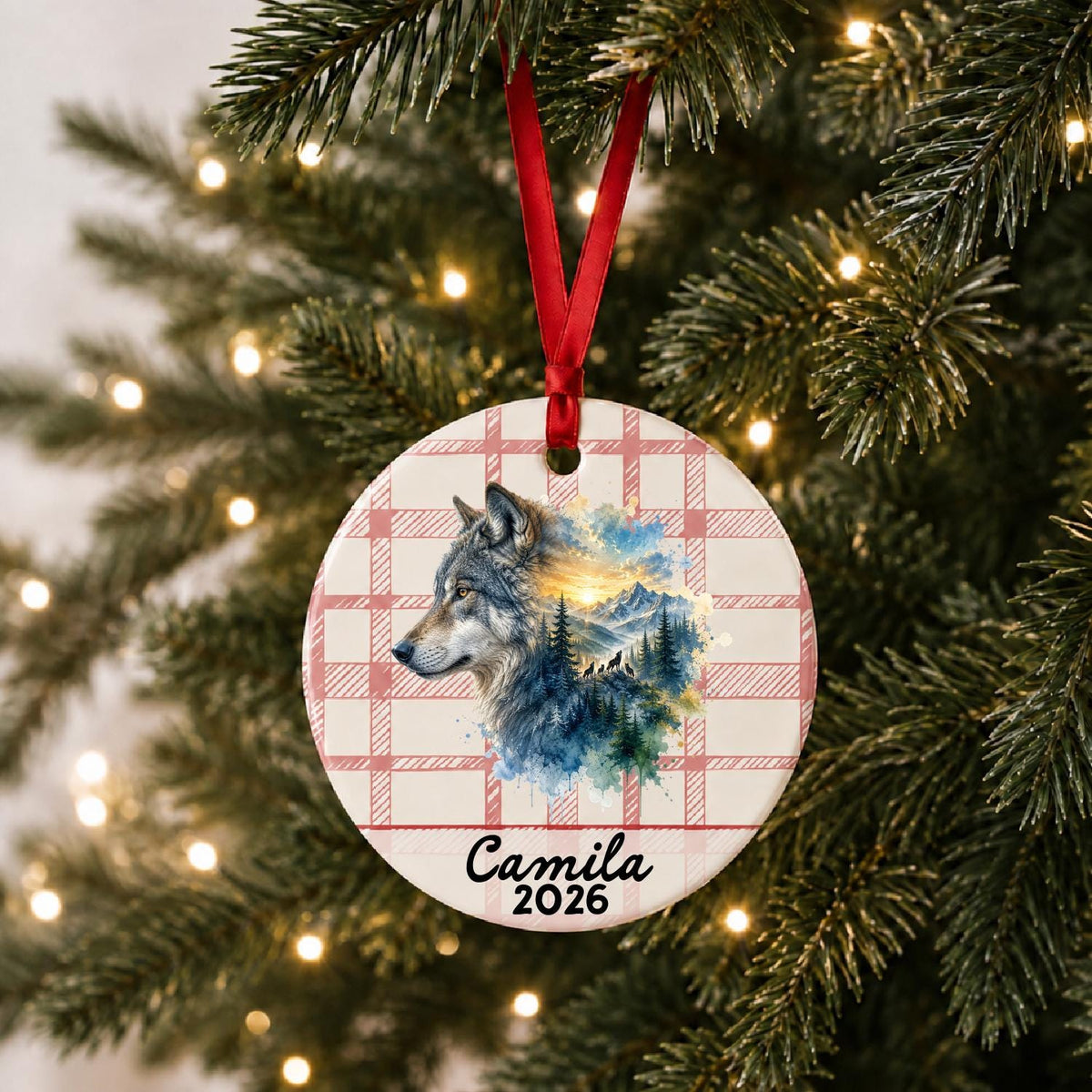 Personalized grey wolf ceramic ornament with name and year on red plaid hanging on a lit Christmas tree