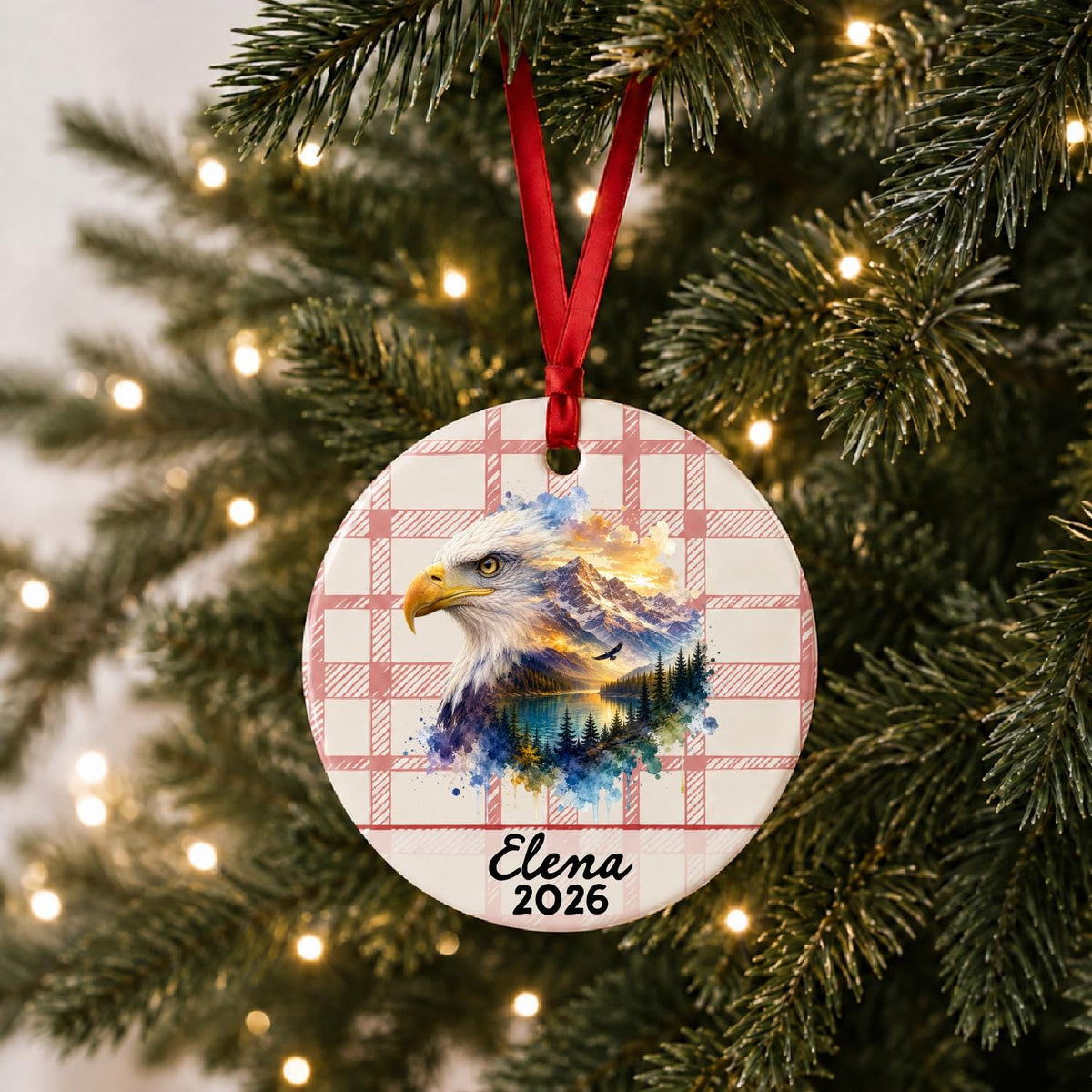 Personalized bald eagle ceramic ornament with name and year on red plaid hanging on a lit Christmas tree