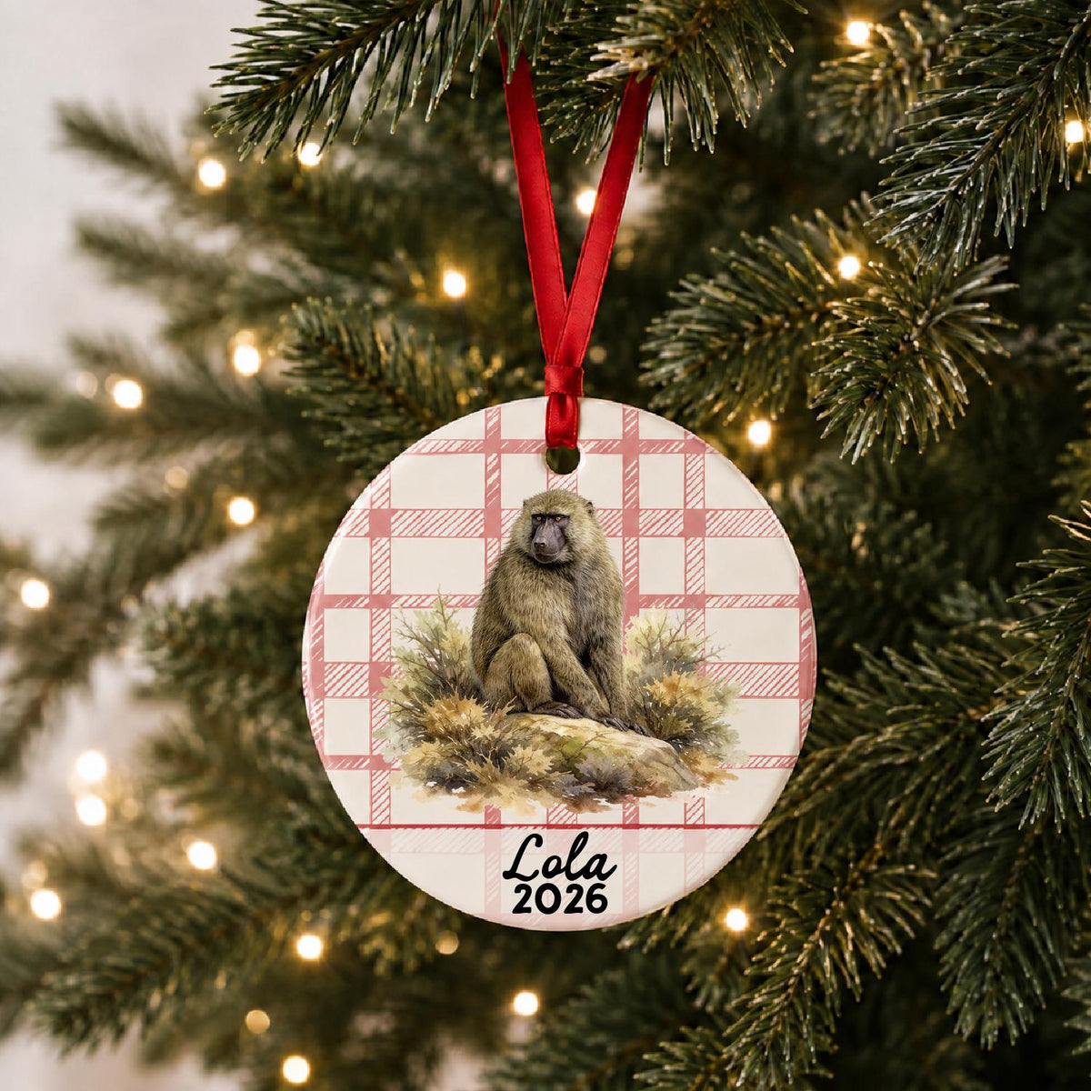 Personalized baboon ceramic ornament with name and year on red plaid hanging on a lit Christmas tree