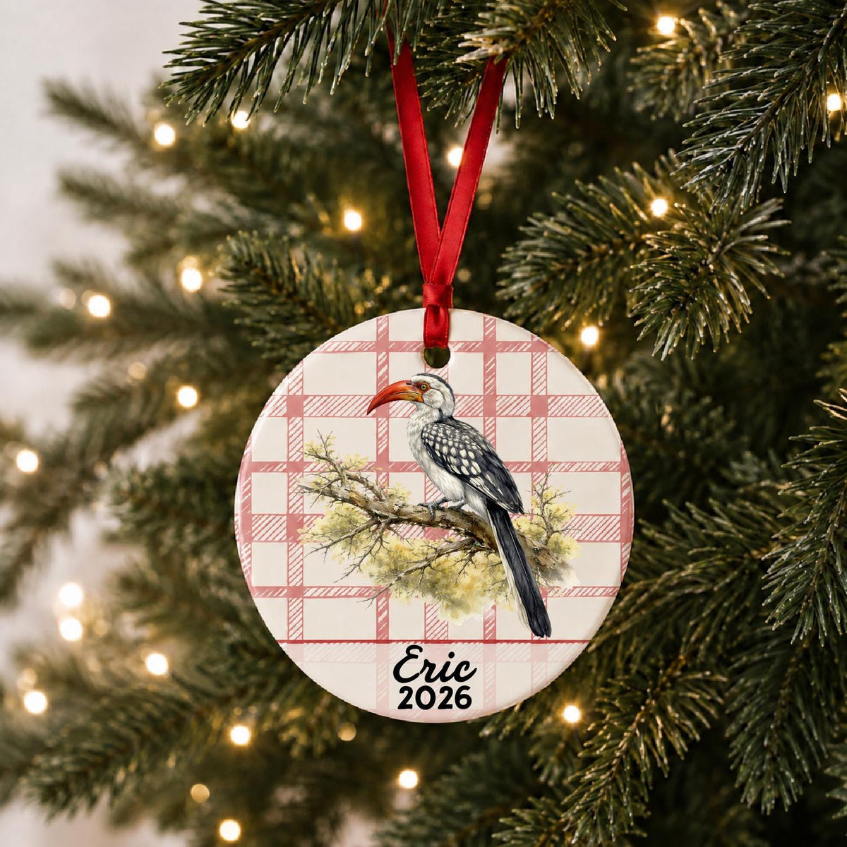Personalized hornbill ceramic ornament with name and year on red plaid hanging on a lit Christmas tree