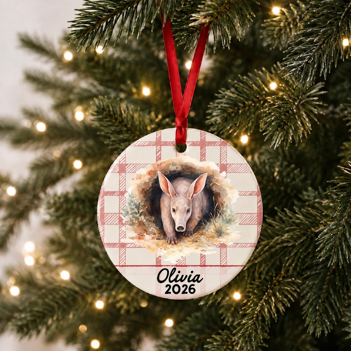 Personalized aardvark ceramic ornament with name and year on red plaid hanging on a lit Christmas tree