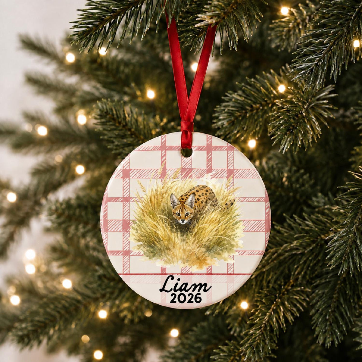 Personalized serval ceramic ornament with name and year on red plaid hanging on a lit Christmas tree