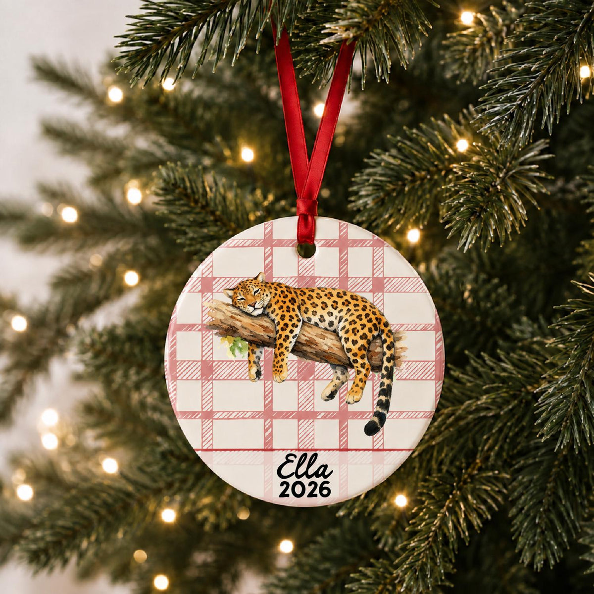 Personalized leopard ceramic ornament with name and year on red plaid hanging on a lit Christmas tree