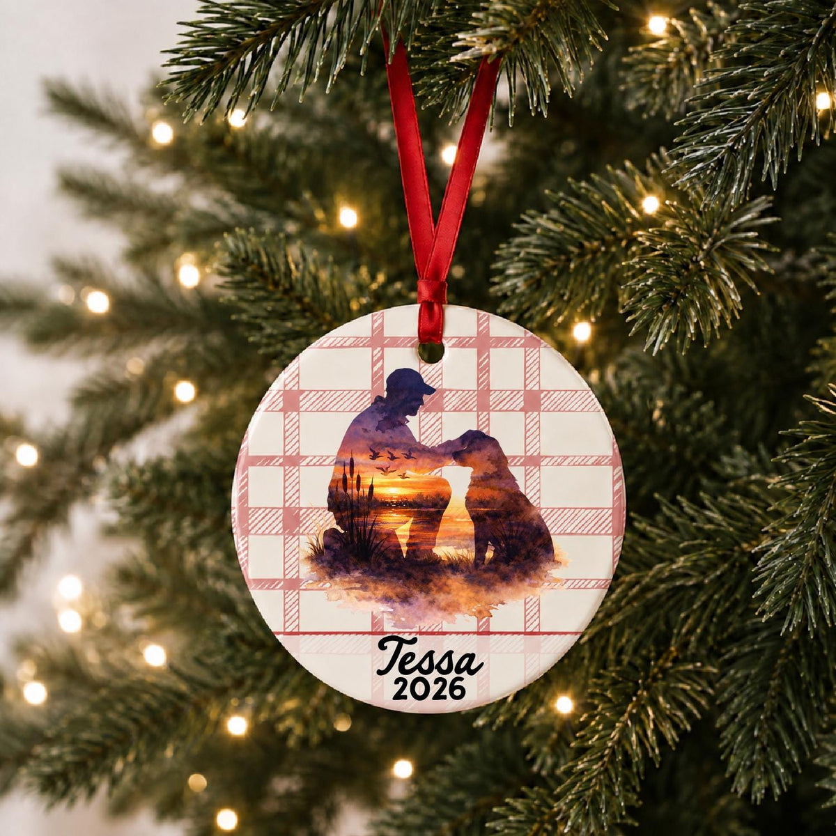 Personalized hunter and dog ceramic ornament with name and year on red plaid hanging on a lit Christmas tree