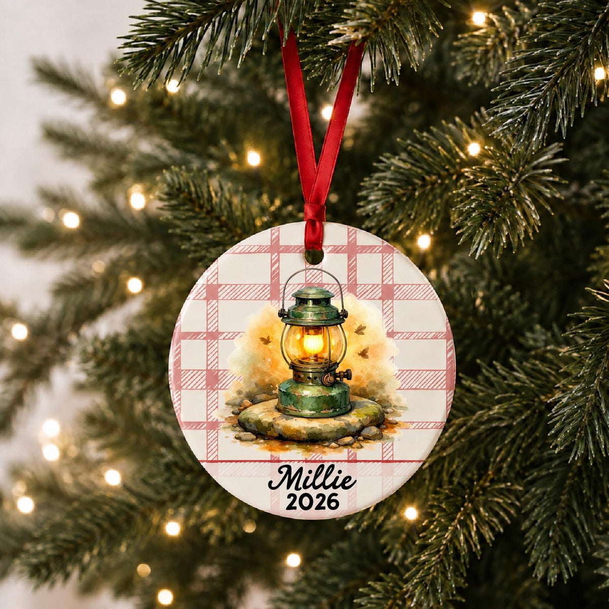 Personalized camping lantern ceramic ornament with name and year on red plaid hanging on a lit Christmas tree