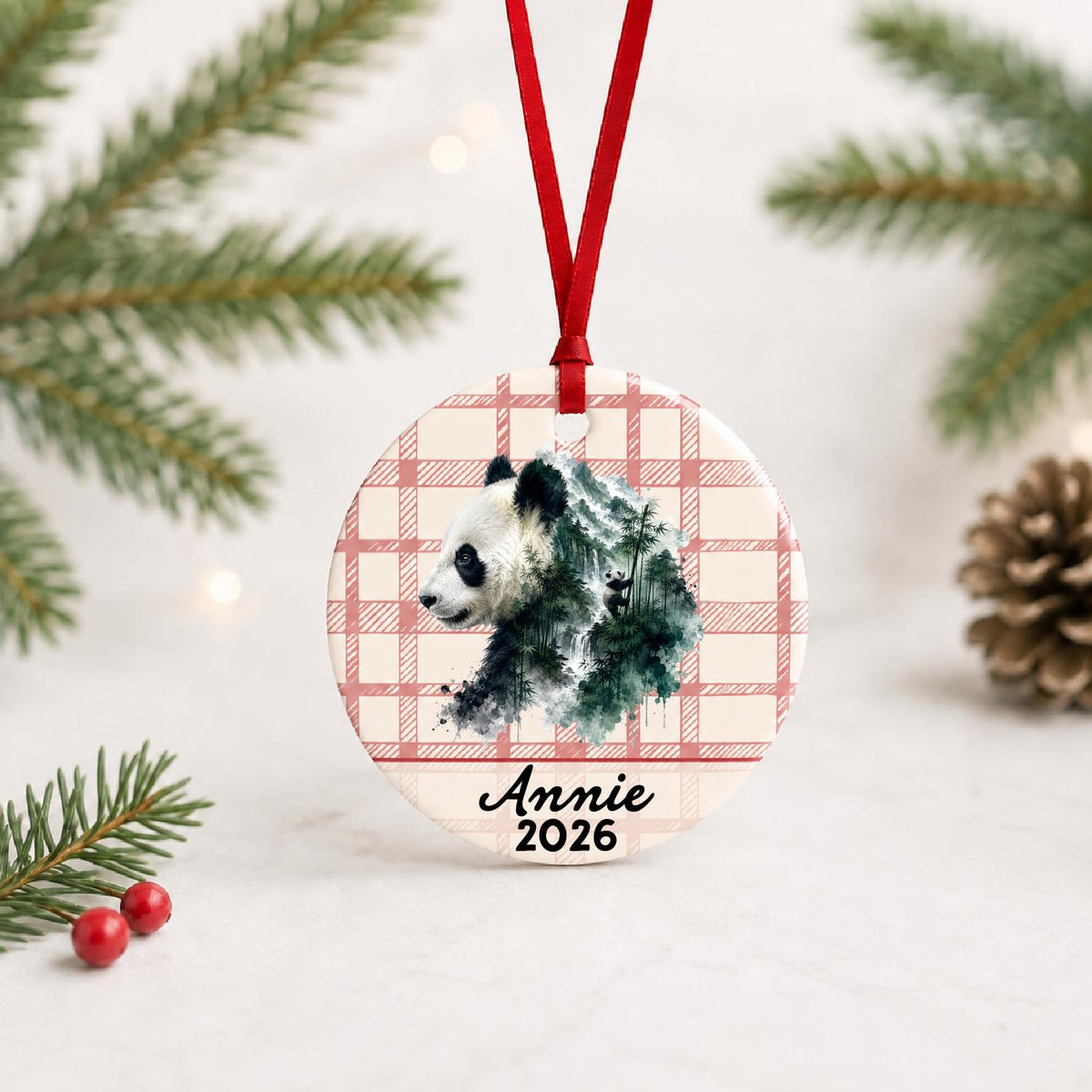 Personalized giant panda ceramic ornament with name and year on red plaid with red ribbon on a white surface with pine branches and pinecones