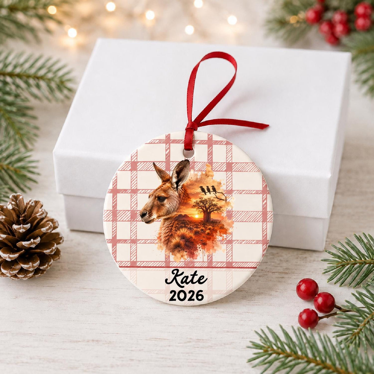 Personalized red kangaroo ceramic ornament with name and year on red plaid in front of a white gift box with pinecones and red berries